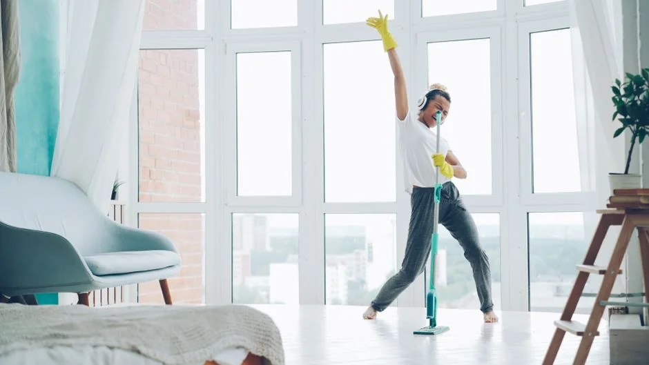 A cleaner in protective coveralls and gloves vacuuming a modern living room.